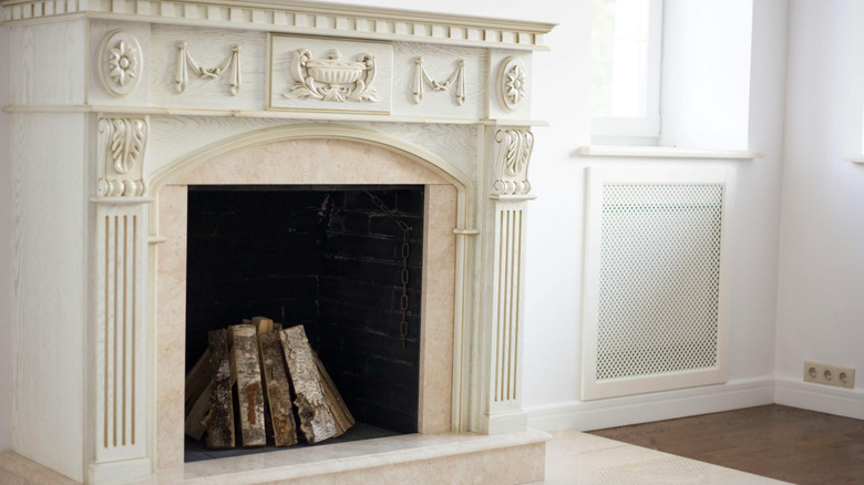 Upright logs inside ornate vintage marble fireplace.