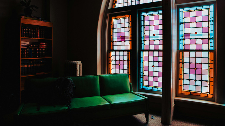 Green leather couch next to three colorful stained glass windows.