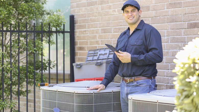 A man standing outside with his hand on an AC unit.