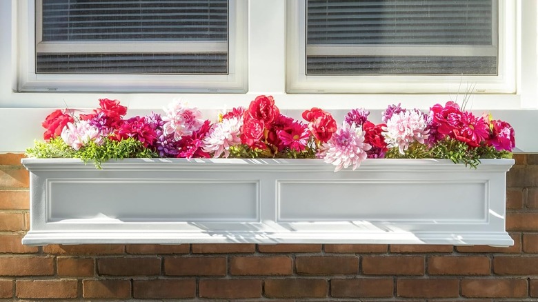 A white flower box mounted below a window is filled with a variety of pink flowers