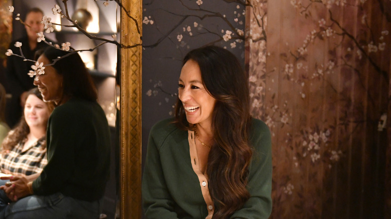 Joanna Gaines sitting in front of a wall painted with cherry blossoms