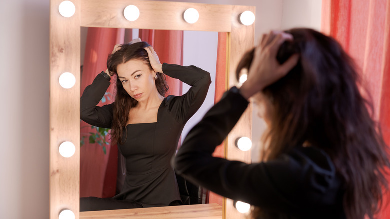 A woman looking at herself in a mirror with bulbs around it