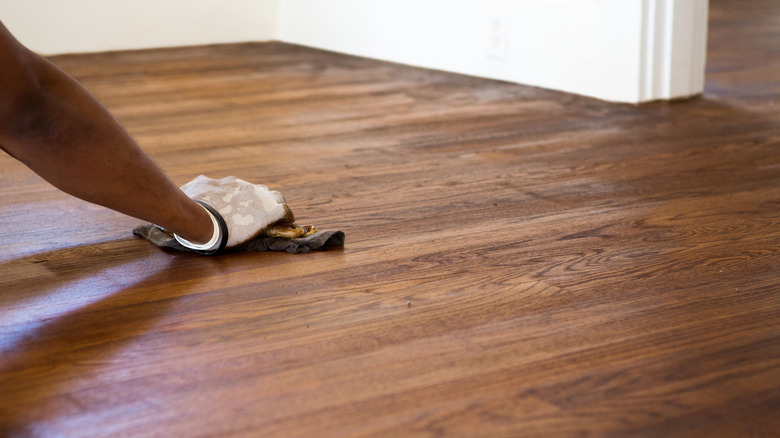 A gloved hand staining a hardwood floor