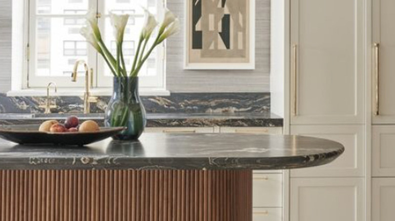 Oval kitchen island with dark gray marble countertop, wood base and brass hardware.