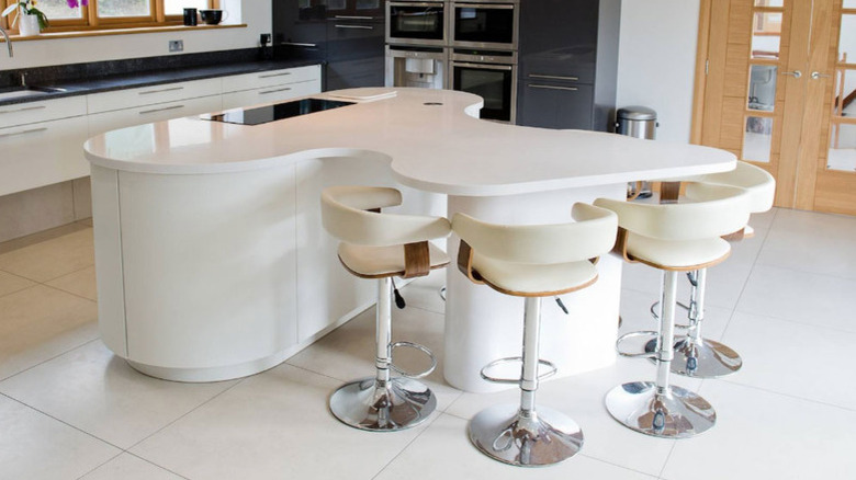Oval kitchen island with curved dining area connected. All white cabinets and countertop.