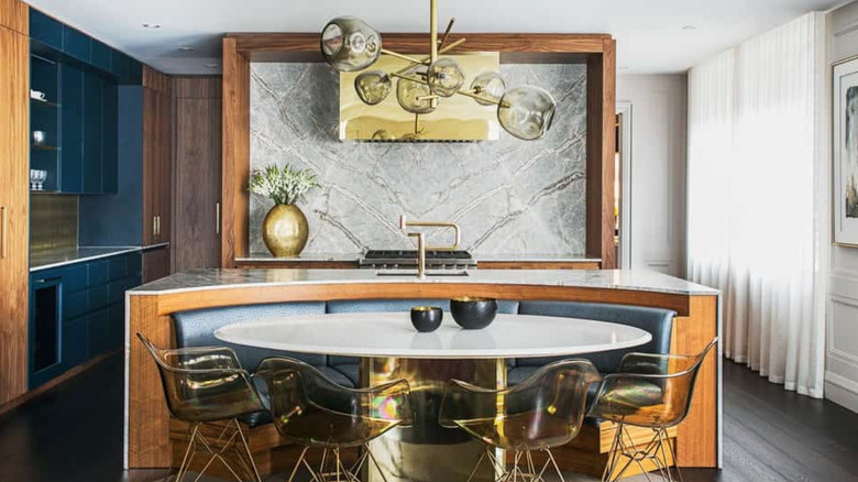 Cut out kitchen island with marble countertop, built-in oval dining booth, white dining table with brass finish base.