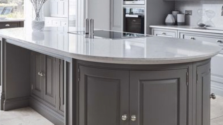 Oval shaped kitchen island with gray cabinets and white countertop.