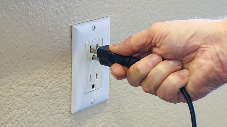 Hand plugging cord into wall socket