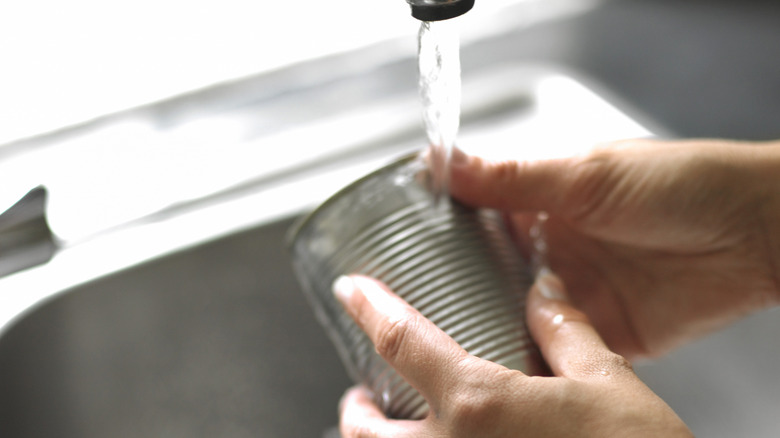 Person rinsing an empty can in a sink