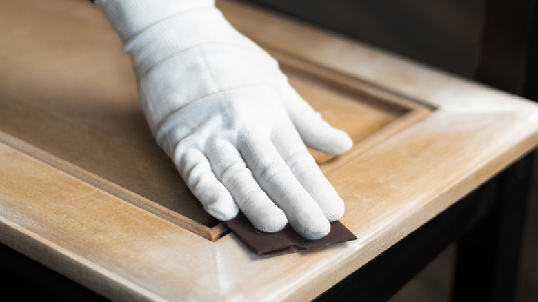 person sanding a wood kitchen cabinet door