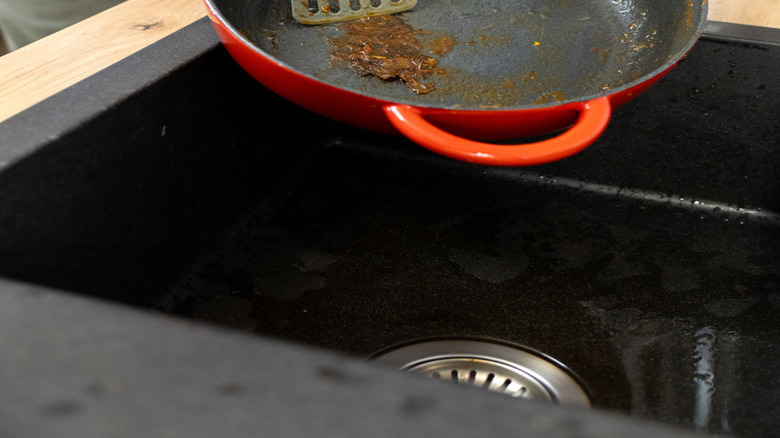 Hands holding pan and scraping burnt-on food with spatula