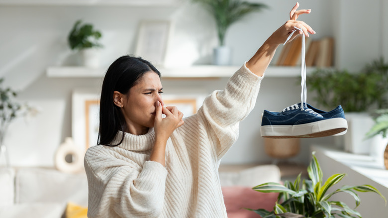 Woman holding stinky shoes by shoestrings and holding nose