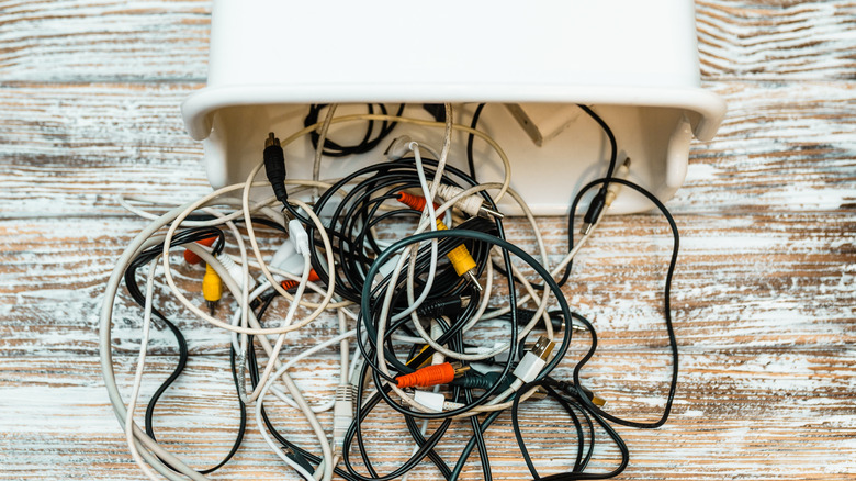 A bunch of cables and cords tangled togeher, dumped out of a container onto a wood surface