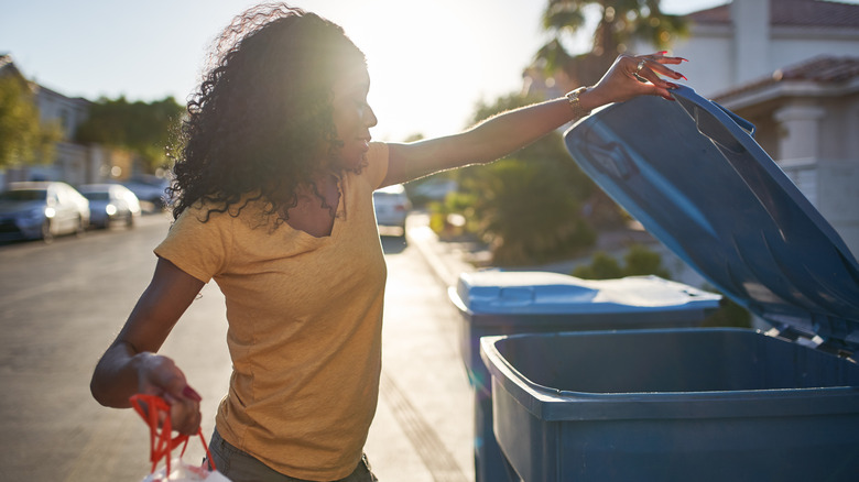 A woman puts a plastic bag in the recycling bin outside her home