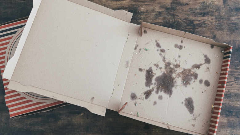 An empty, grease-stained pizza box sitting on a wood surface