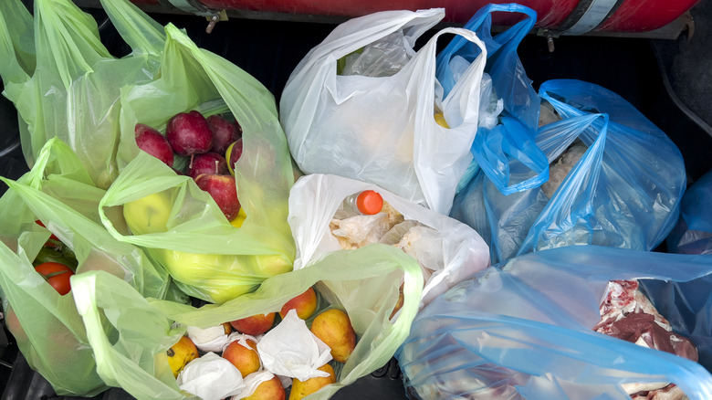 Open trunk of a car filled with plastic shopping bags holding grocery items