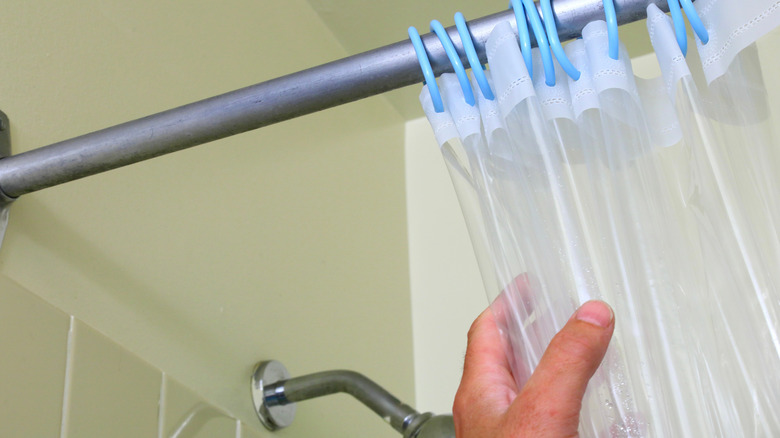 A hand pulls a plastic shower curtain hanging from a rod