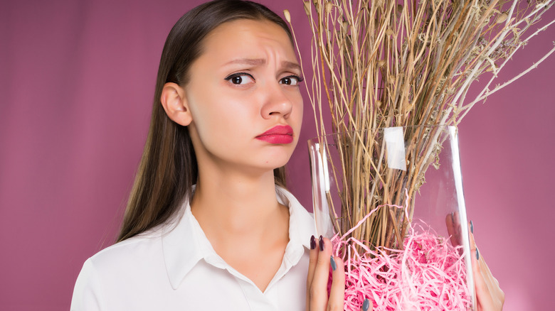 Frustrated woman holding dead potted plant