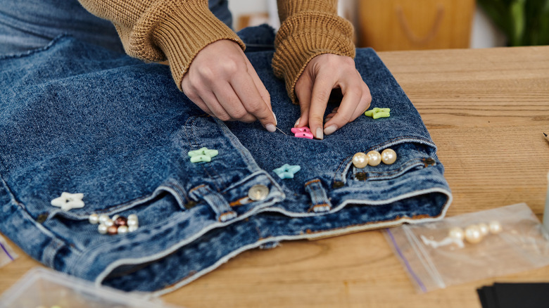 A person sewing buttons onto a pair of jeans