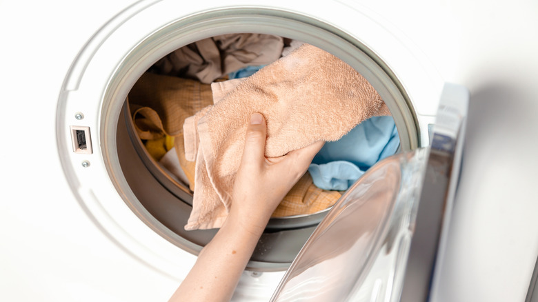 Hand putting several towels in washing machine