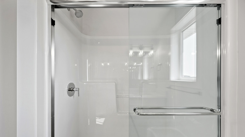 A white fiberglass shower stall with silver fixtures and glass doors