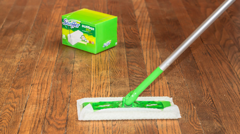 A Swiffer Sweeper with a dry cloth on wood floor, with the product box in the background