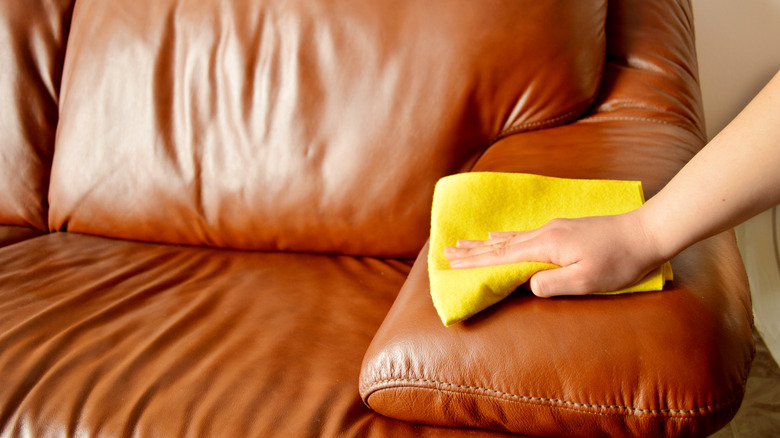 Person wiping a brown leather couch with a cloth