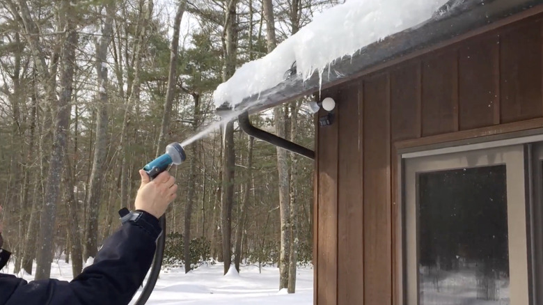 Man melting ice dam with hot water from hose
