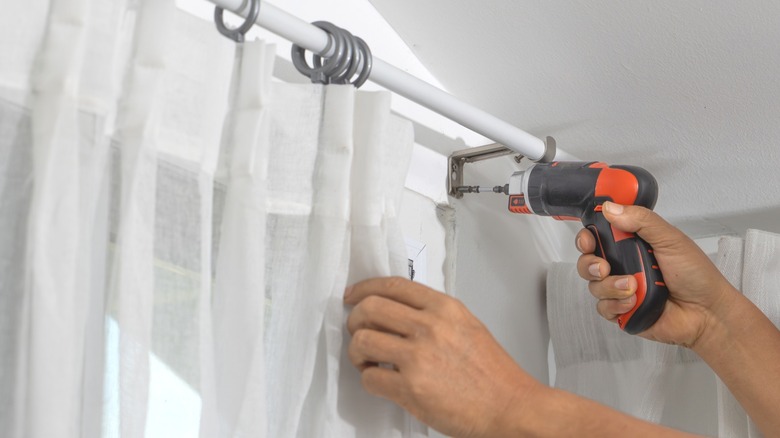 a person installs a curtain rod with sheer white drapes