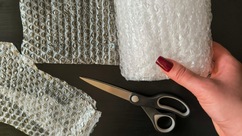 woman holding a roll of bubble wrap with a pair of scissors that were used to cut off a piece