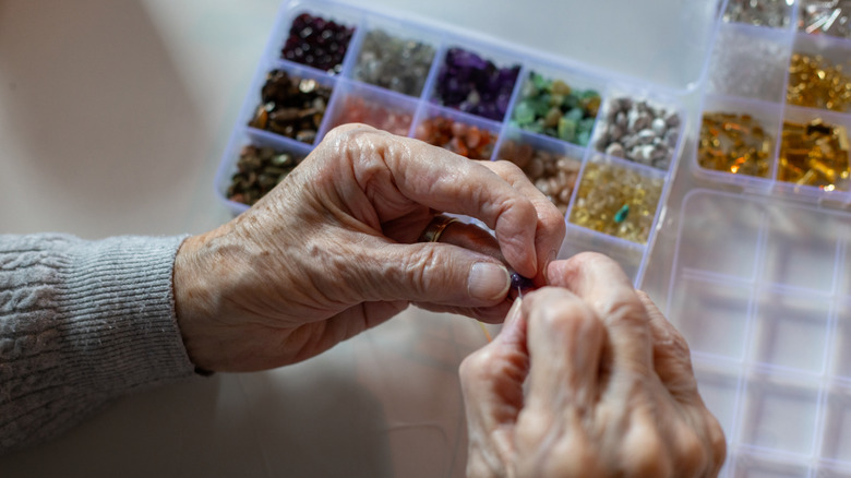 Elderly hands are shown stringing brightly colored beads