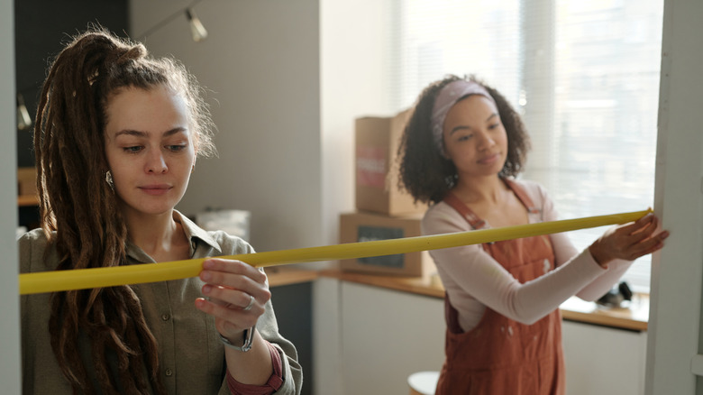 Two smiling women measure a large doorway
