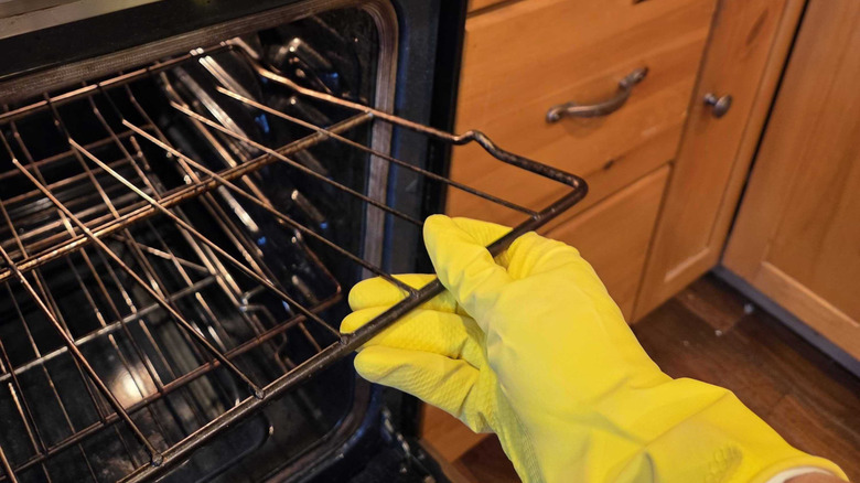 a person wearing rubber gloves removes a dirty rack from the oven.