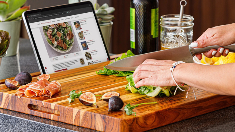 Hands cutting on Teakhaus cutting board, following recipe from tablet