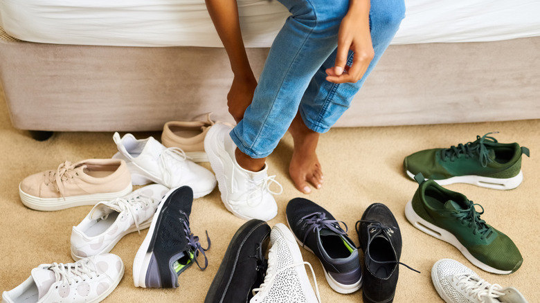 Woman trying on a sneaker with her feet surrounded by pile of shoes