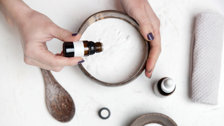 Hands adding drops of essential oil into bowl of baking soda.