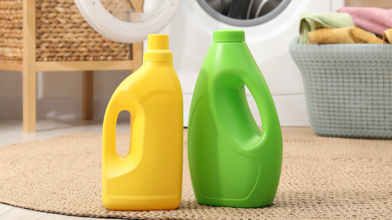 Pair of generic green and yellow laundry detergent containers on laundry room rug by machine