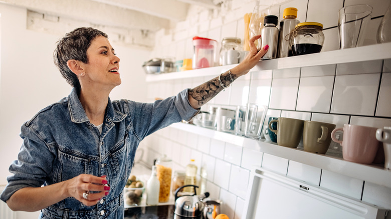 Woman getting bottle from plain white kitchen shelves