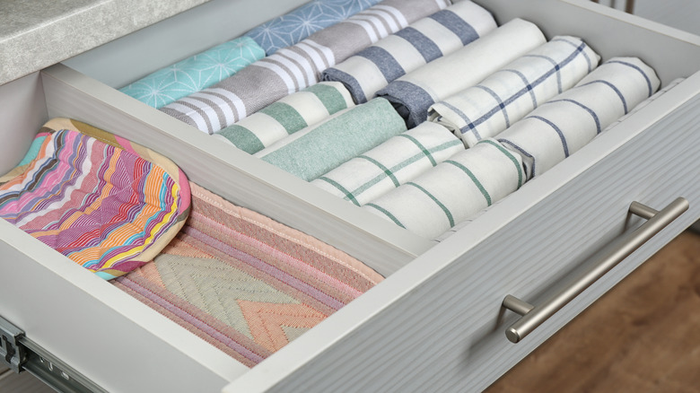 Rolled kitchen towels separated from pot holders by a drawer divider