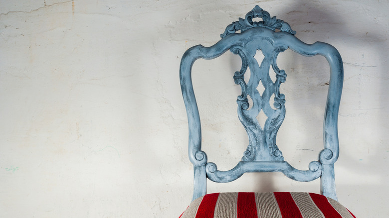An antique wooden chair painted blue with red and white striped upholstery on the seat.