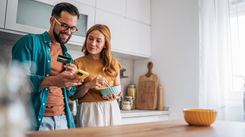A smiling couple stands in a light-filled kitchen