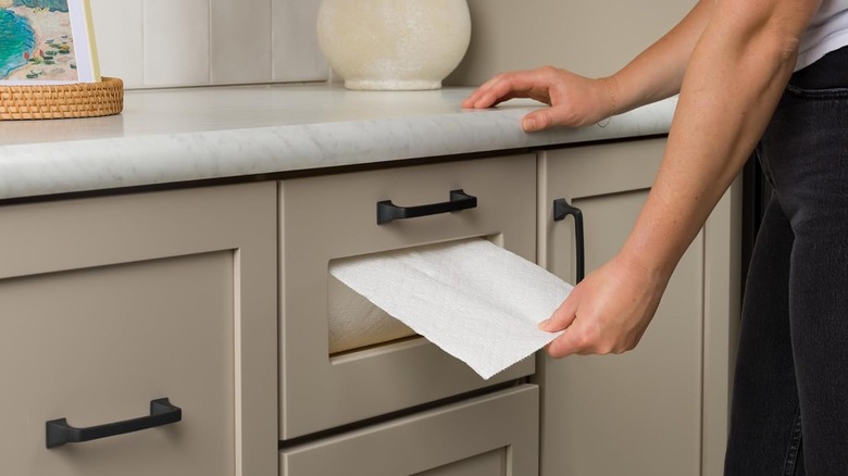 person removing a paper towel sheet from a closed paper towel storage drawer