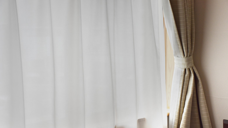 A window covered with a sheer curtain; a blackout curtain is pulled to the side