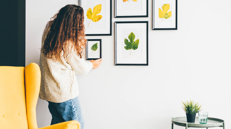 Person hanging wall art in front of yellow chair
