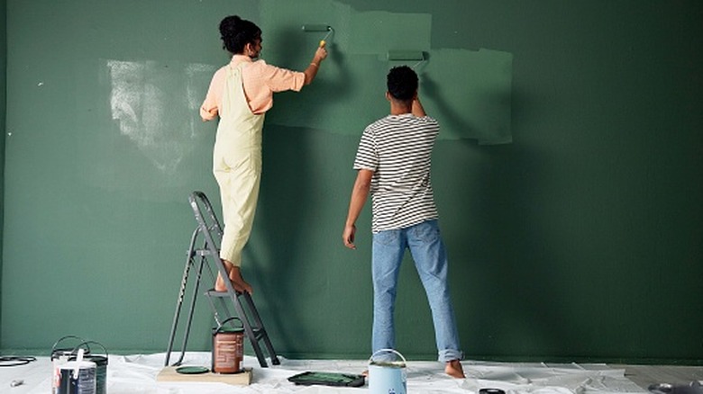 Couple painting a wall dark green