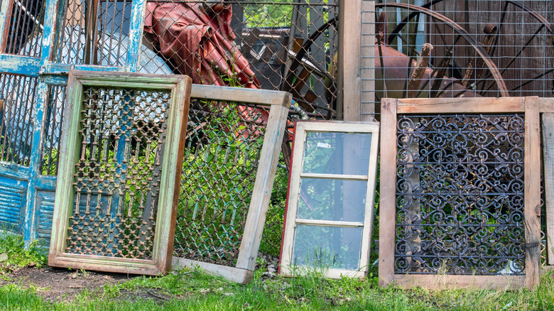 Vintage windows and screens lean against a fence at a salvage yard.