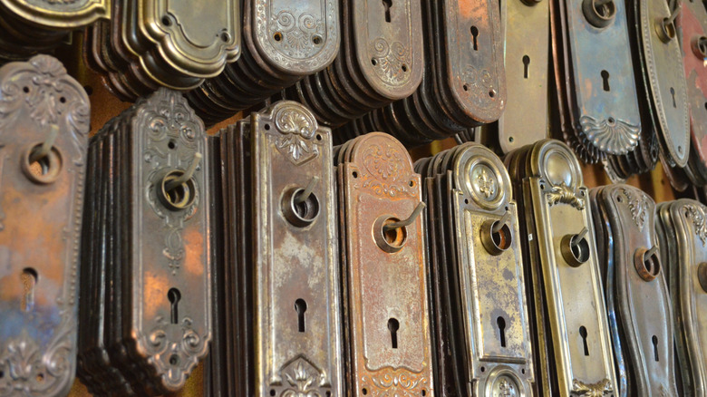 Dozens of antique doorknob plates hang on a wall.
