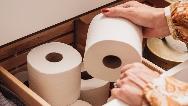 A woman's hands reaching for a wooden drawer of toilet paper
