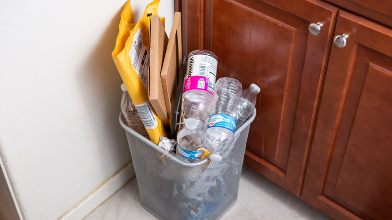 An overflowing trashcan sits next to cherry kitchen cupboards