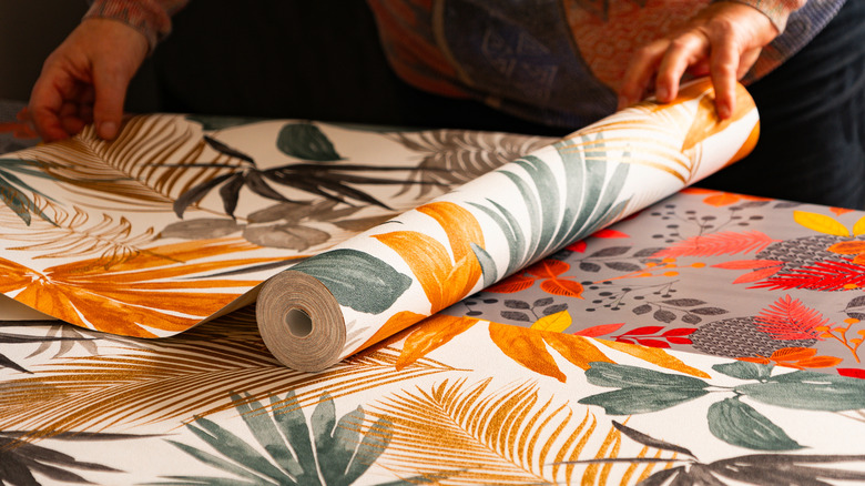 A person unrolls colorful peel-and-stick wallpaper on a table